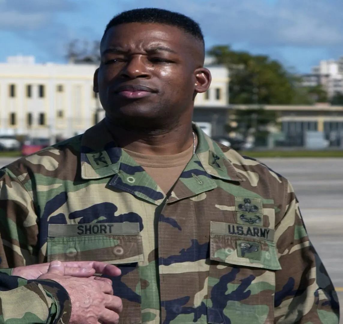 A man in military fatigues standing next to buildings.