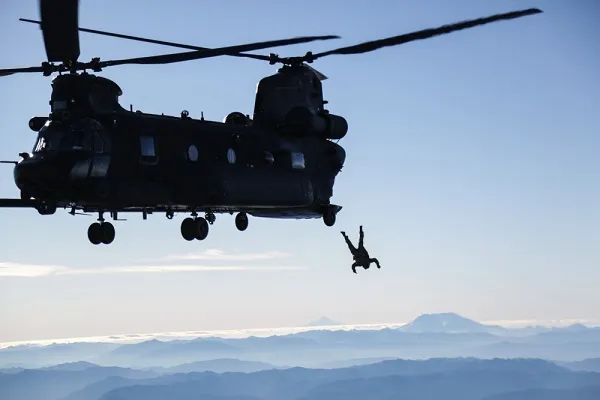 A person is hanging from the back of a helicopter.