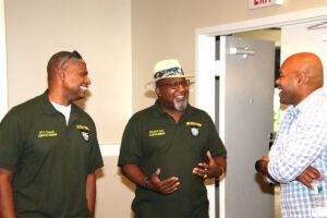 Two men in green shirts and a man with a hat