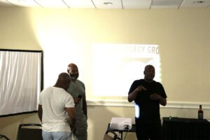 A group of men standing in front of a projector screen.