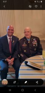 Two men sitting at a table with one of them wearing an army uniform.