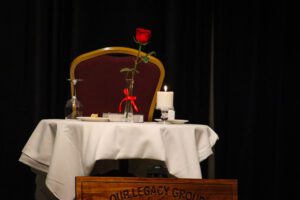 A table with a red rose on it and a white tablecloth.