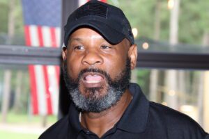 A black man with a beard in front of an american flag.
