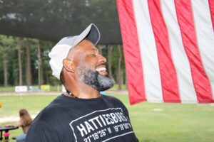A man with a beard smiling in front of an american flag.