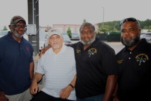 Four men posing for a photo in a parking lot in color