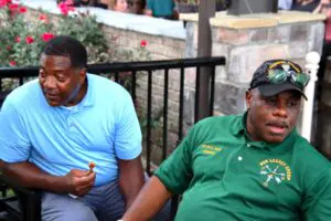 Two men in green shirts sitting on a bench in color image