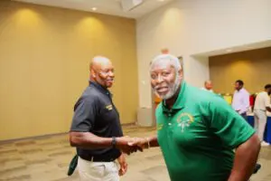 Two men in green shirts shaking hands in a room.