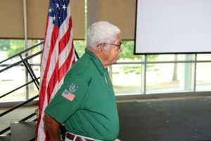 A man in a green shirt standing in front of an american flag.