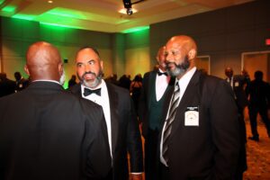 A group of men in tuxedos talking to each other in color image